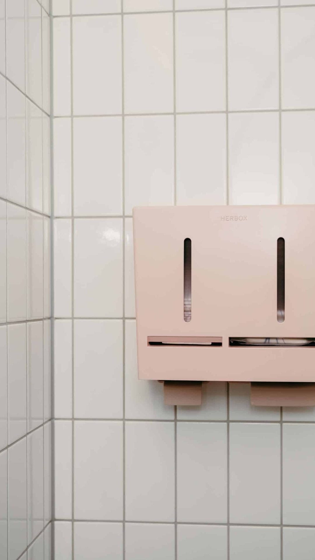 Herbox rosa dispenser på kakelvägg - Mensskydd för gäster och kunder