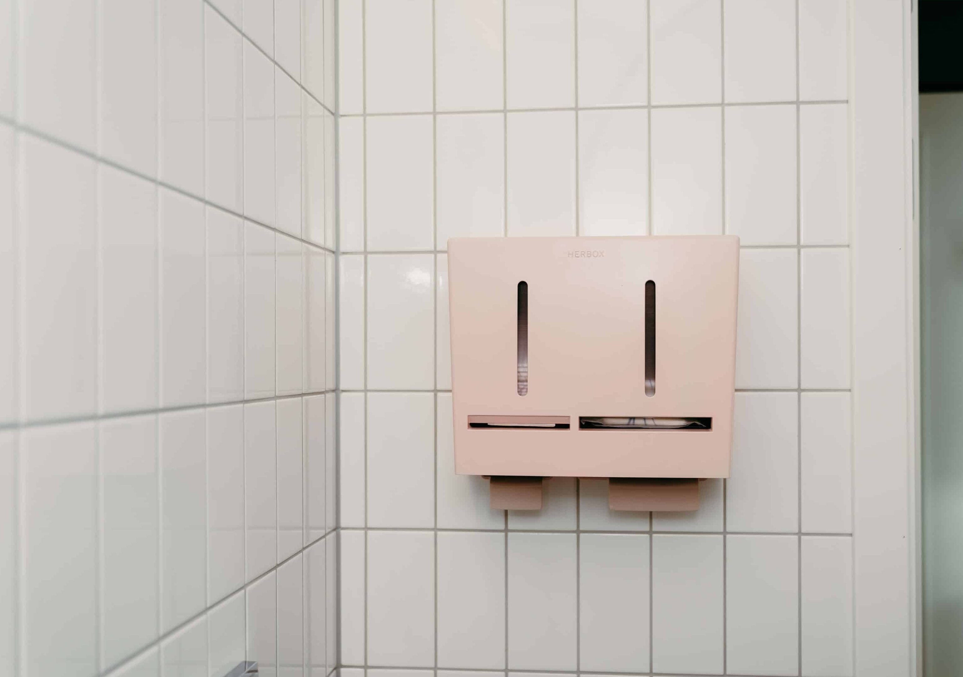 Herbox rosa dispenser på kakelvägg - Mensskydd för gäster och kunder