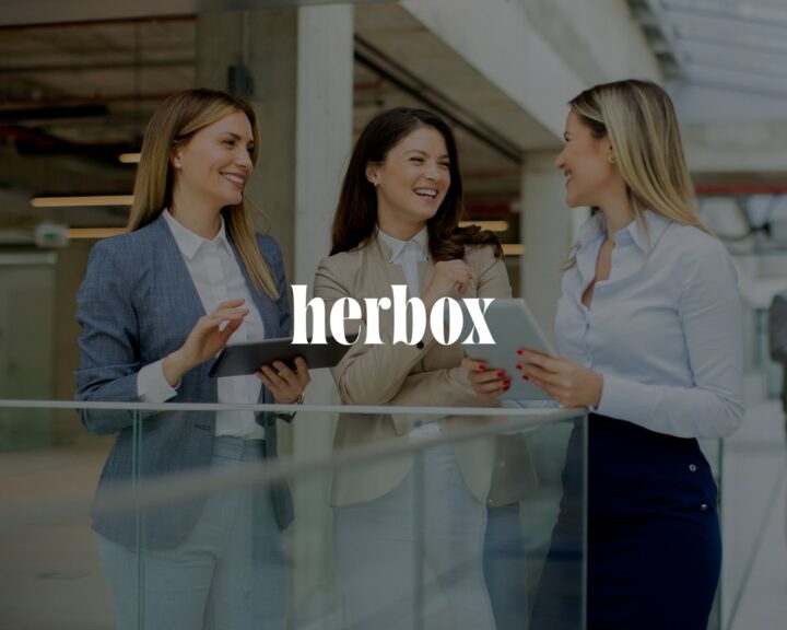 Tre kvinnor i affärskläder pratar och håller digitala surfplattor. Texten "herbox" syns över bilden.