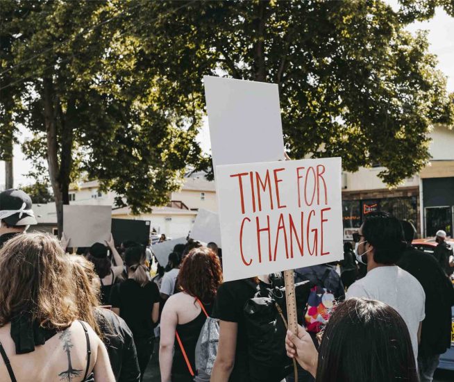 Kvinnor och män som gemensamt går i ett demonstrationståg med en skylt med texten "Time for change".