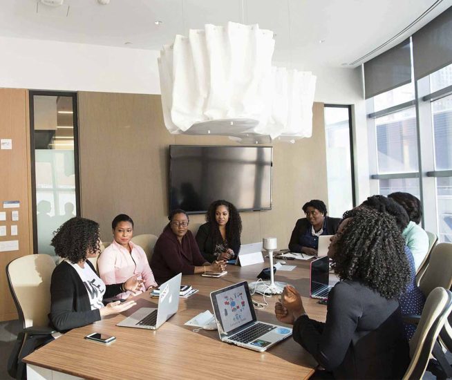 Sju affärskvinnor kvinnor som sitter runt ett bord i ett konferensrum. De har ett affärsmöte.