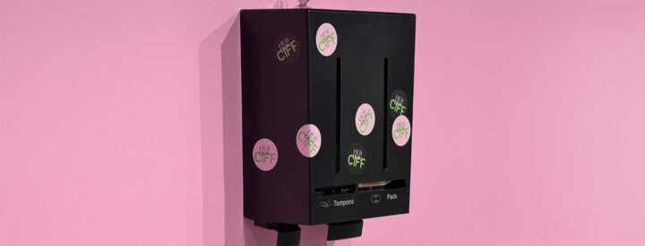 Svart Herbox hygienautomat på rosa vägg med CIFF och Herbox klistermärken.