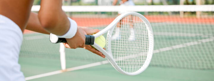 Bild på en tennisbana där en kvinna står redo för att serva med ett vitt tennisrack