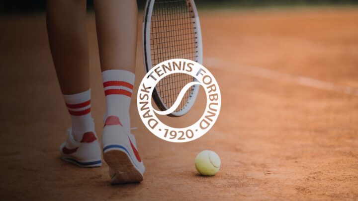 Tennisspillerens ben, ketcher, bold og Dansk Tennis Forbunds logo på en grusbane.