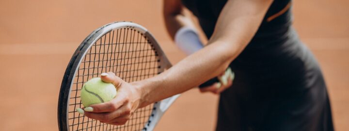 En person i sportsdragt holder en tennisketcher og bold klar til at serve på en tennisbane.