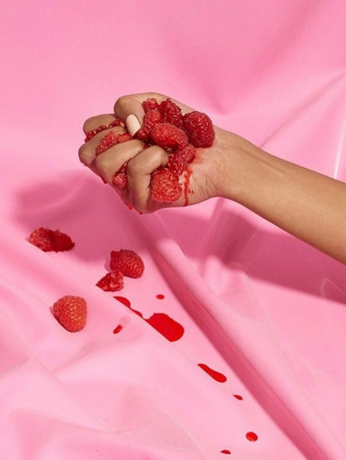 Hand krossar hallon över ett rosa underlag, med saftspill.