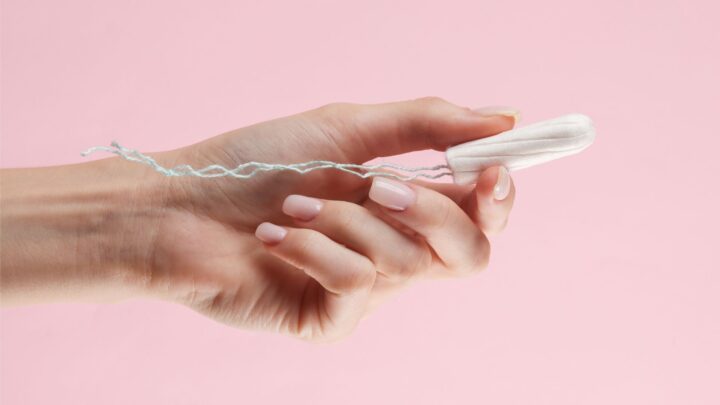 Hand holding a tampon against a pink background.