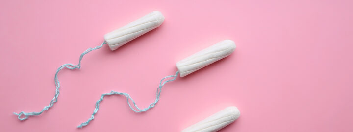 Three white tampons with blue strings on a pink background.