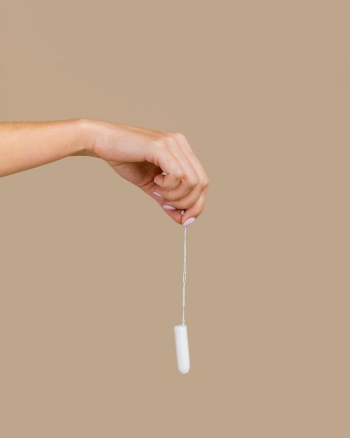 A hand holding a tampon by the string against a beige background.