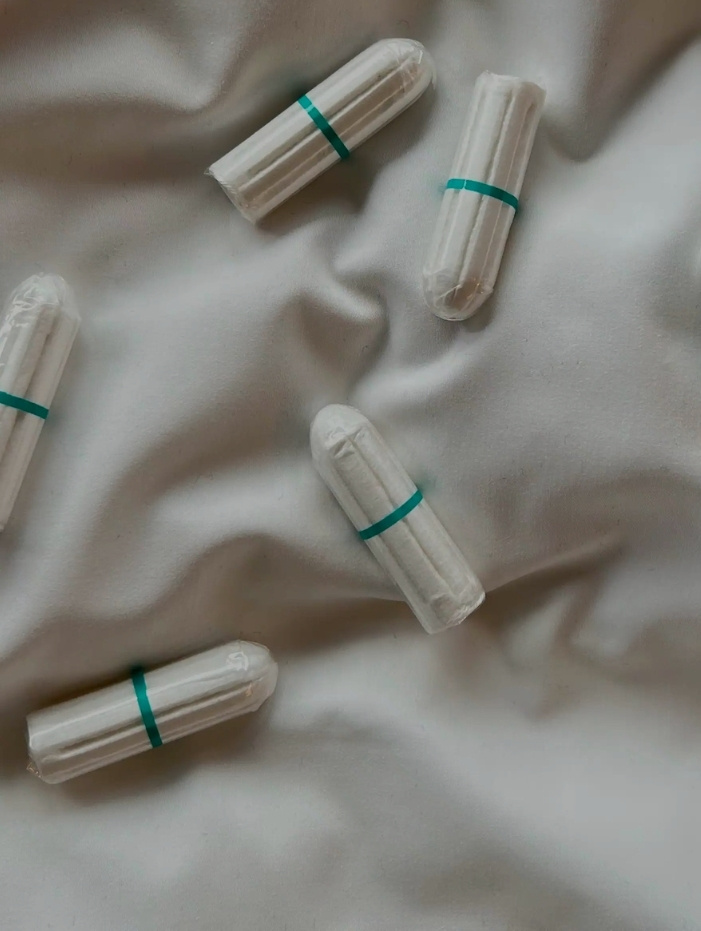 Sex vita ekologiska tamponger med gröna band ligger på ett skrynkligt vitt tyg.
