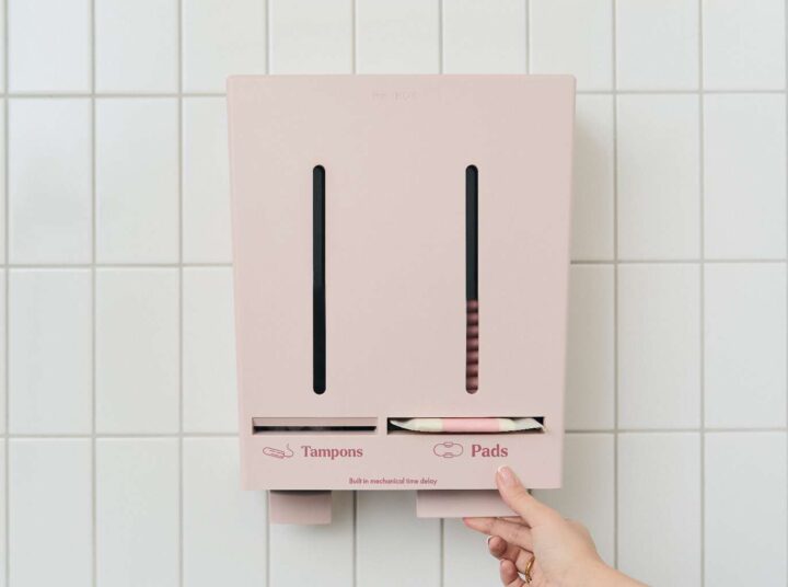 Close-up van een Herbox-dispenser waarbij een hand een maandverband uit de machine haalt