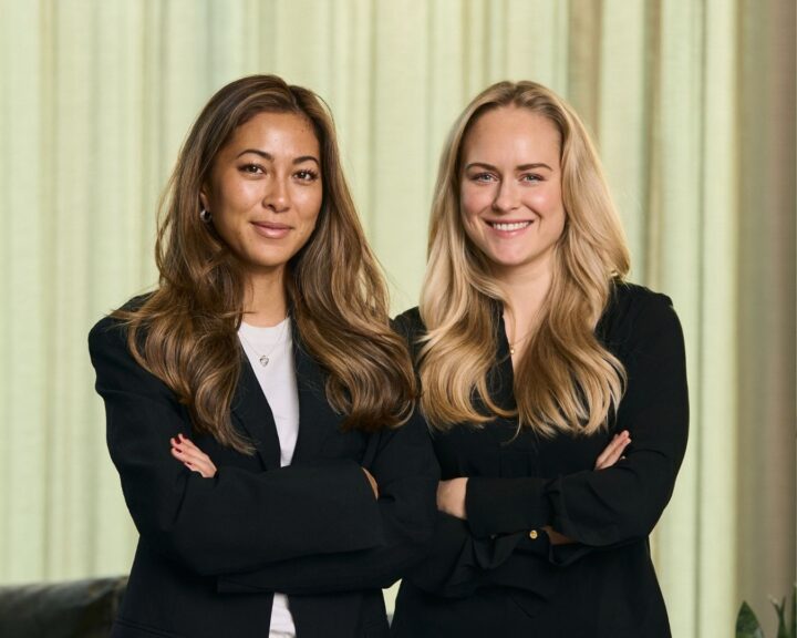 Hanna & Linn in zwarte kleding met gevouwen armen, glimlachend naar de camera.