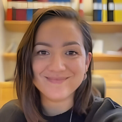 Maria Lindermann People Experience Advisor på Mondelez Sverige som ler med hyllor och färgglada pärmar i bakgrunden.