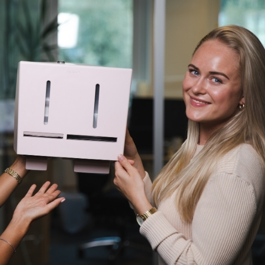 Een vrouw houdt een roze apparaat met twee sleuven vast, terwijl een andere hand het ondersteunt, in een kantooromgeving.