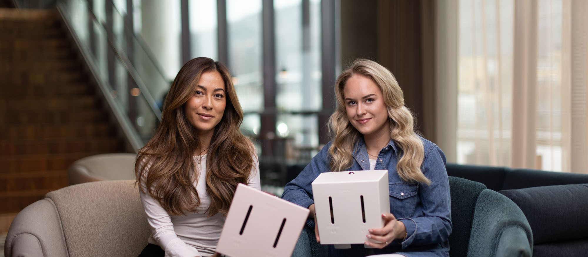 Hanna en Linn, oprichters van Herbox, tonen twee menstruatieproducten dispensers in roze en wit