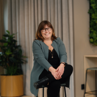 Pernilla Sundén, HR-Chef på Holtab Group sitter leende på en stol, med grönska och gardin i bakgrunden.
