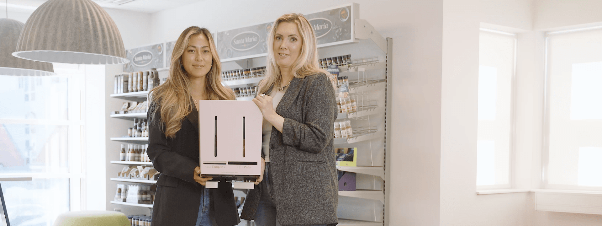 Hanna från Herbox och Eva Berglie från Paulig håller en Herbox dispenser för mensskydd.