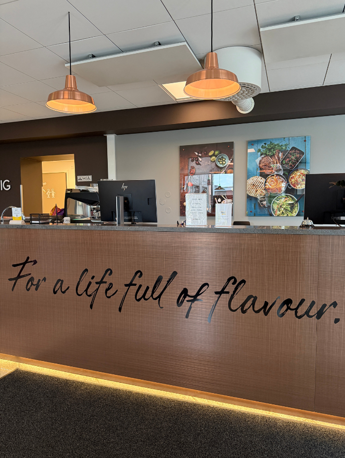 Reception med träpanel, texten "For a life full of flavour", två lampor ovan och matbilder på väggen.